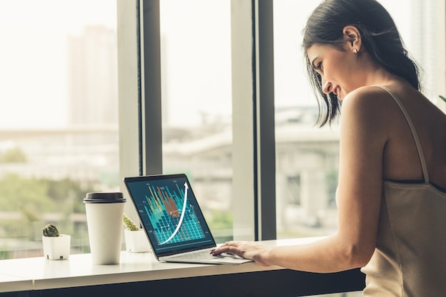 Une femme sourit en analysant des graphiques boursiers ascendants sur la plateforme de trading la plus populaire au monde depuis son ordinateur portable.