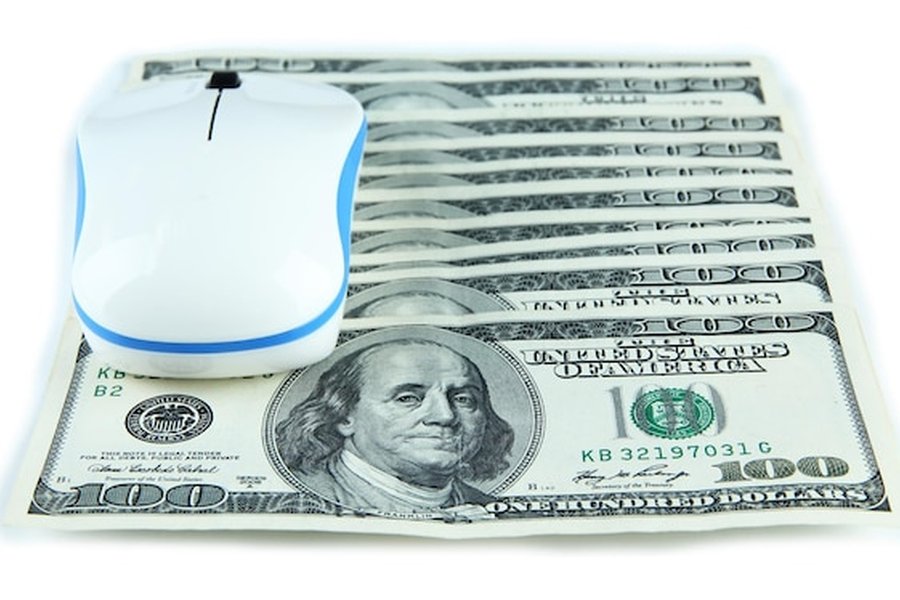 Une souris d'ordinateur blanche posée sur une liasse de billets de cent dollars, représentant l'évolution numérique d'un stablecoin adossé au dollar.