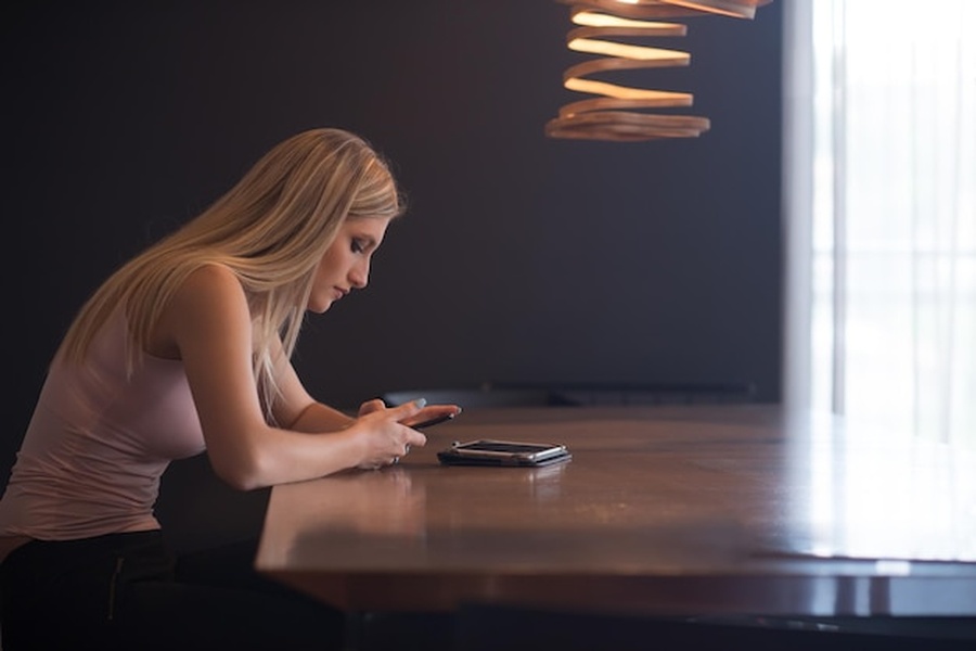 Une femme blonde analyse les marchés financiers sur son smartphone via la meilleur plateforme de trading pour débutant depuis son salon.