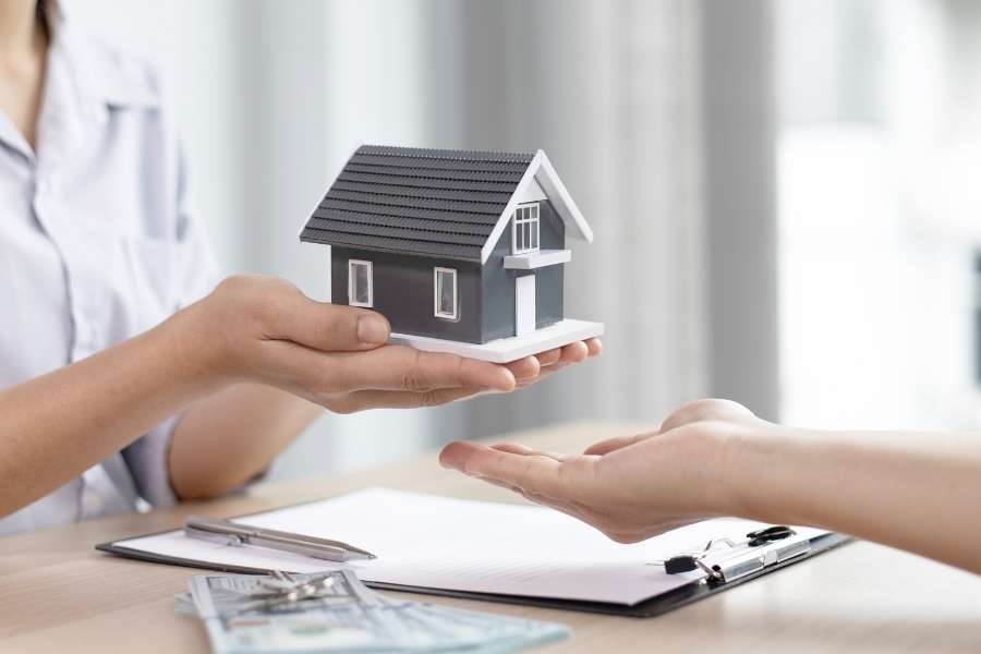 Une personne présente une maquette de maison grise pour illustrer l'achat d'un bien en copropriété.