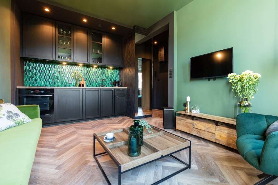 Un salon moderne avec des murs verts, un parquet et une cuisine ouverte optimisée grâce au home staging.