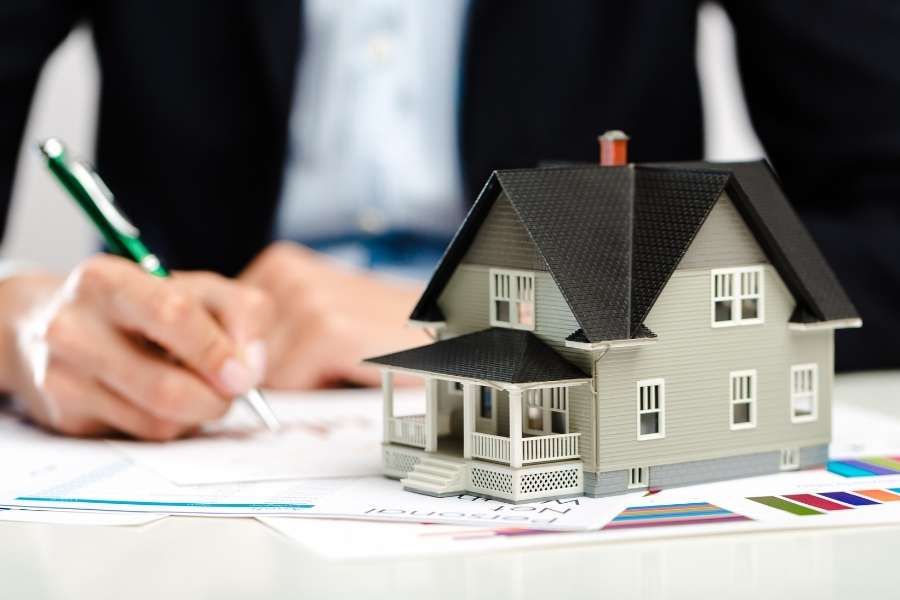 Une personne signe des documents professionnels à côté d'une maquette de bâtiment pour un investissement en immobilier industriel.